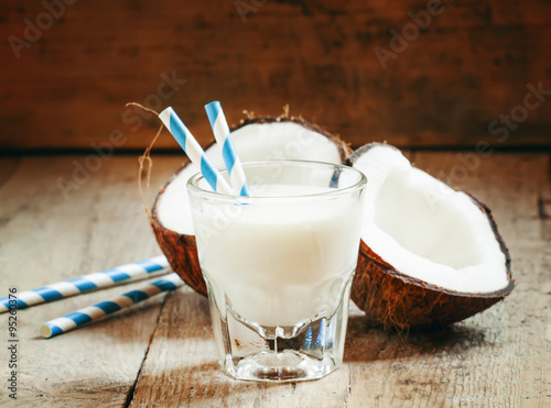 Coconut milk in a glass with striped straw and coconut halves, s