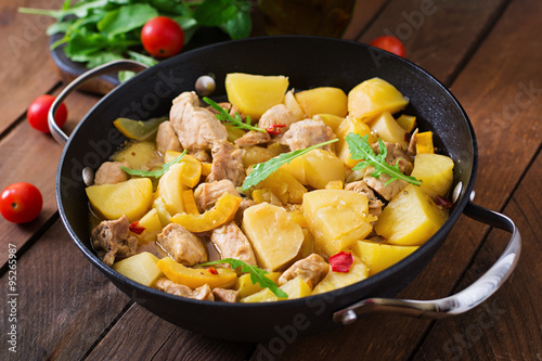 Stewed potatoes with meat and vegetables in a roasting tin on a wooden background
