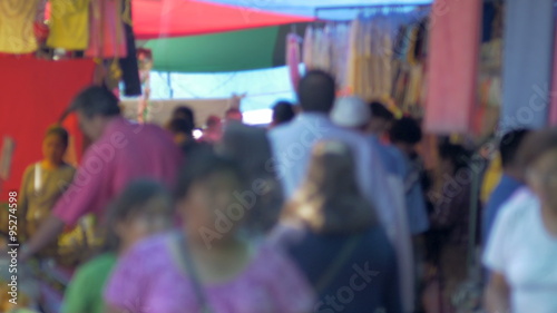 A crowded outdoor market in a latino country busy with shoppers walking by the camera out of focus.