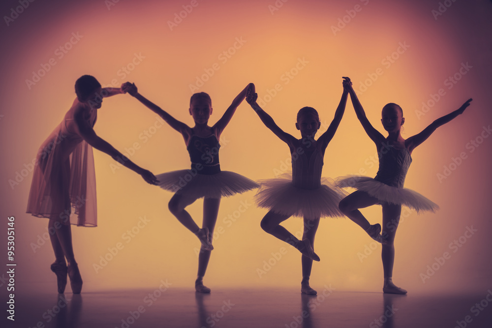 Three little ballerinas dancing with personal ballet teacher in dance studio