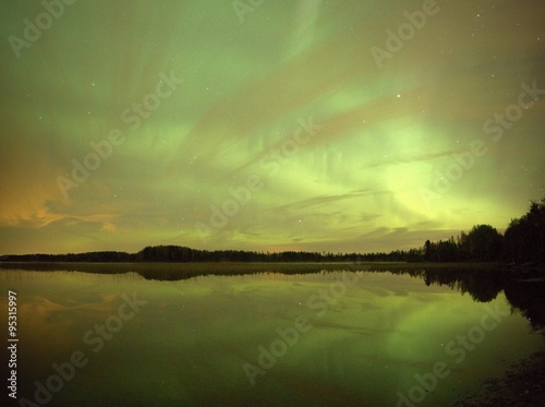Northern lights (Aurora Borealis) in the night sky over a beautiful lake in Finland. Vibrant green colors on the sky and reflections on the still water of the lake.