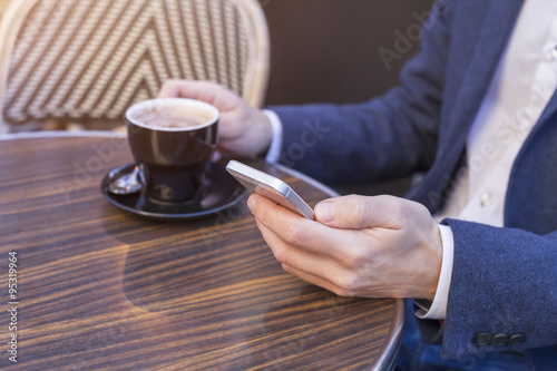 Young adult using mobile phone on restaurant terrace with coffee