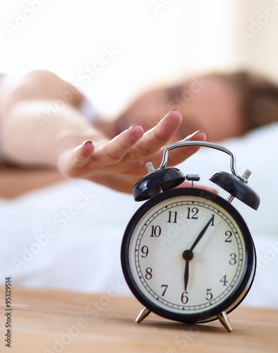 Young sleeping woman and alarm clock in bedroom at home