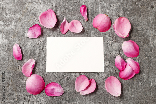 Blank card among rose petals on grey stone background