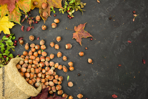 Hazelnuts in a sack with autumn leaves and dried berries, space for text.