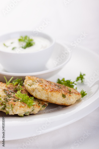 Cabbage pancakes with parsley and yogurt dressing on a white plate. Top view.