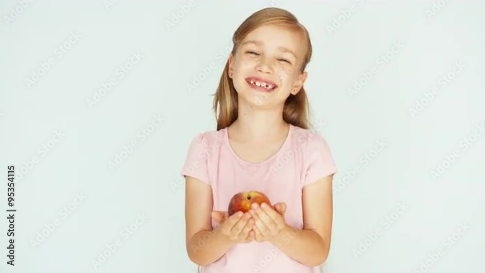 Child holding peach on the white background. Girl sniffing peach and smiling at camera Child holding peach on the white background. Girl sniffing peach and smiling at camera