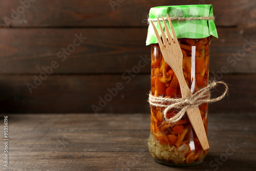 Delicious marinated mushrooms in glass jar on wooden background