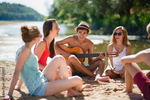 Teenagers having fun at the beach, are singing with guitare