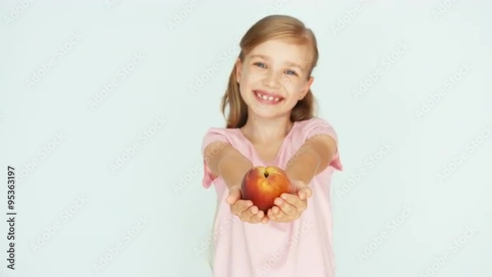 Child showing peach on the white background. Girl sniffing and holding peach and smiling at camera Child showing peach on the white background. Girl sniffing and holding peach and smiling at camera
