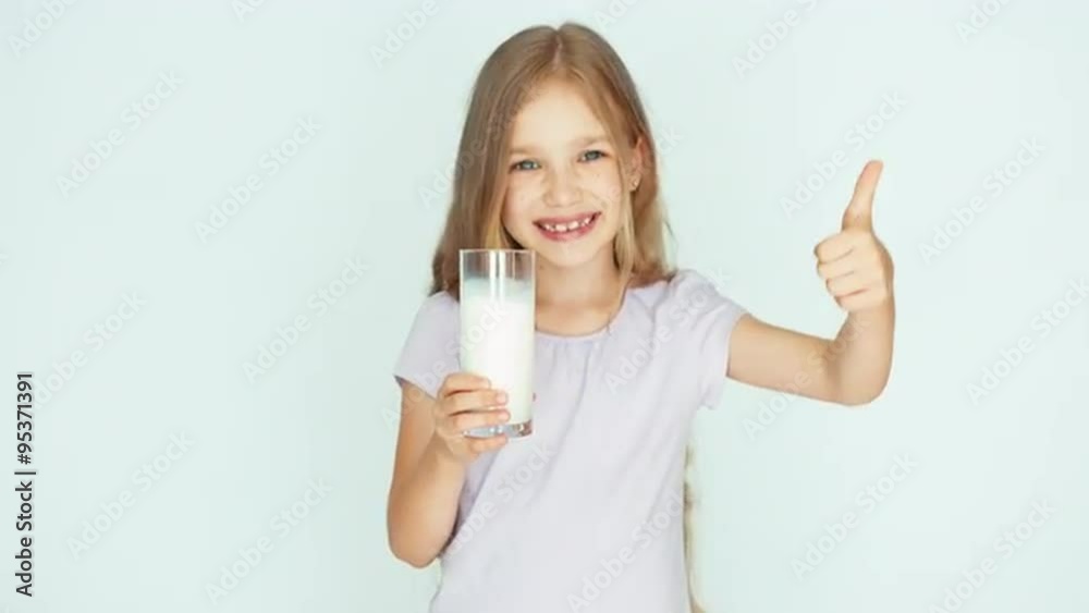 Child sniffing milk. Girl showing glass of milk at camera. Girl with beautiful blond hair on a white background. Thumb up. Ok Child sniffing milk. Girl showing glass of milk at camera. Girl with beautiful blond hair on a white background. Thumb up. Ok