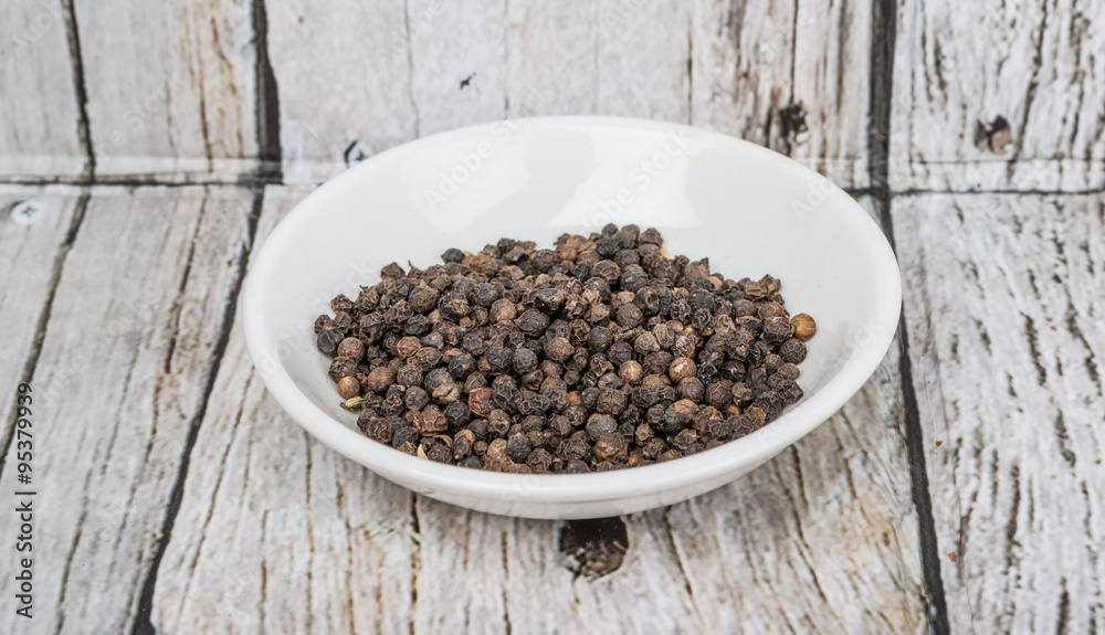 Black peppercorn in white bowl over wooden background Black peppercorn in white bowl over wooden background