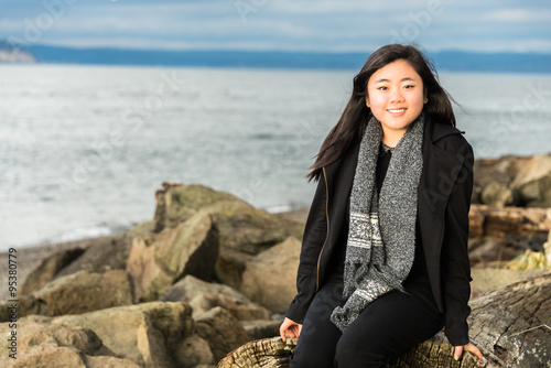 Beautiful Smiling Young Woman Sitting on Beach Driftwood. Copy space.
