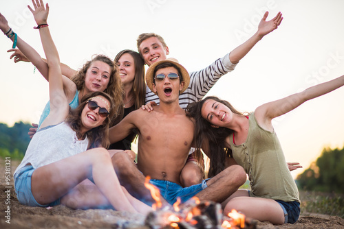 trendy teenagers on the beach at sunset around a wood fire 