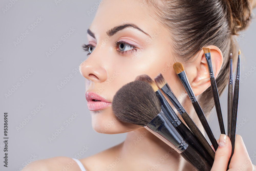 Beauty girl with makeup brushes. Perfect smooth skin.Applying makeup.Beautiful young woman holding different make up brushes Beauty girl with makeup brushes. Perfect smooth skin.Applying makeup.Beautiful young woman holding different make up brushes