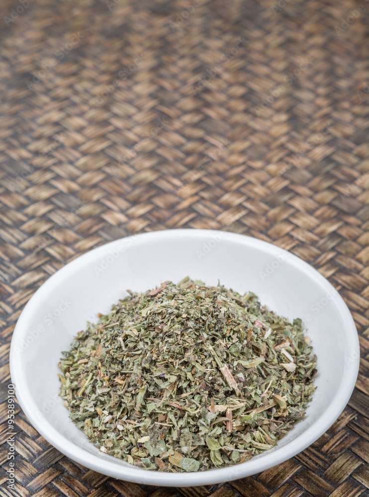 Dried lemon balm leaves in white bowl over wicker background Dried lemon balm leaves in white bowl over wicker background