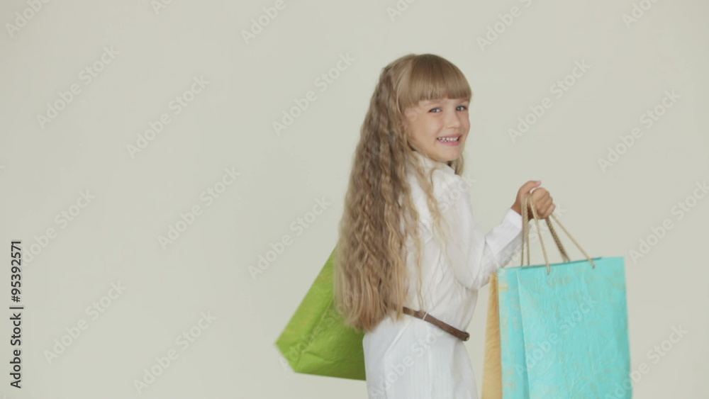Cheerful funny little girl standing with multicolored paper bags in her hands smiling and laughing at camera Cheerful funny little girl standing with multicolored paper bags in her hands smiling and laughing at camera