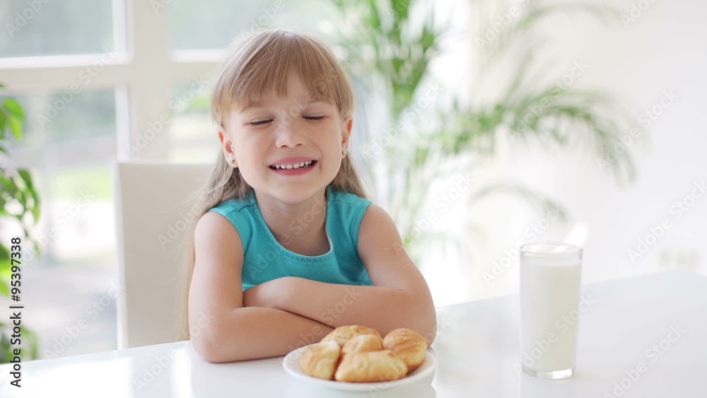 Cute little girl sitting at table with plate of cakes and glass of milk in front of her and smiling Cute little girl sitting at table with plate of cakes and glass of milk in front of her and smiling