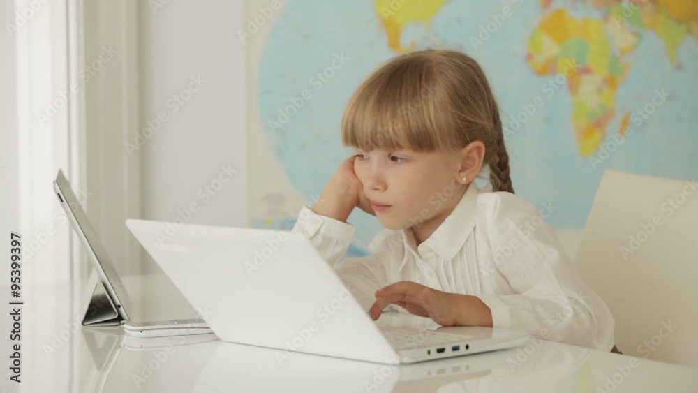 Funny little girl sitting at table studying with laptop and smiling at camera Funny little girl sitting at table studying with laptop and smiling at camera
