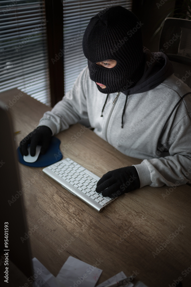 masked thief sitting in front of computer masked thief sitting in front of computer