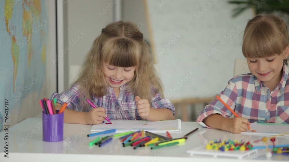Two little girls drawing with colored pencils at drawing class and smiling at camera Two little girls drawing with colored pencils at drawing class and smiling at camera