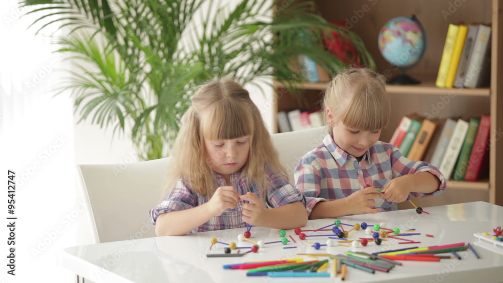 Two little girls sitting at table playing with logic toys and smiling at camera Two little girls sitting at table playing with logic toys and smiling at camera