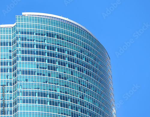 Top section of modern office building from glass and metal with many large panoramic windows in business cluster vertical front view closeup