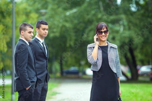 Attractive new female coworker passing by two young businessmen on the street