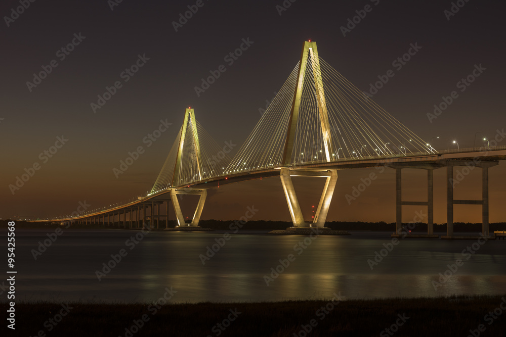 Fototapeta premium Most Arthura Ravenela Jr. oświetlony na tle ciemniejącego nieba o zmierzchu. Most prowadzi przez osiem pasów ruchu na rzece Cooper między Charleston i Mount Pleasant, Karolina Południowa.