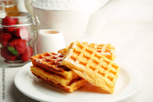 Sweet homemade waffles with fresh strawberries on plate, on light background