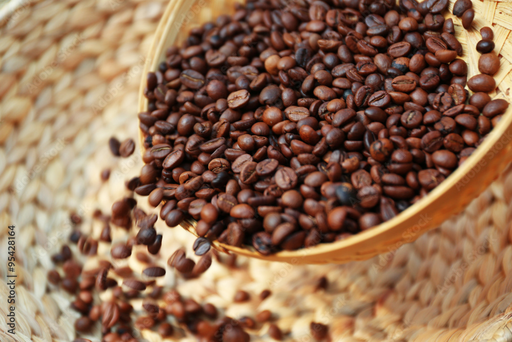 Fototapeta premium Roasted coffee beans scatter from wattled basket into the other one
