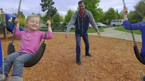 Cute little girls smile big while being pushed by their dad on a swing