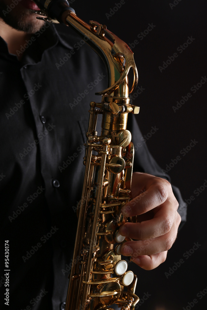 Obraz premium Musician in black shirt with sax on dark background, close up