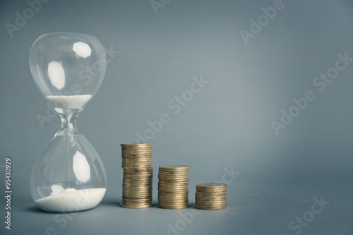 Hourglass with coins on gray background