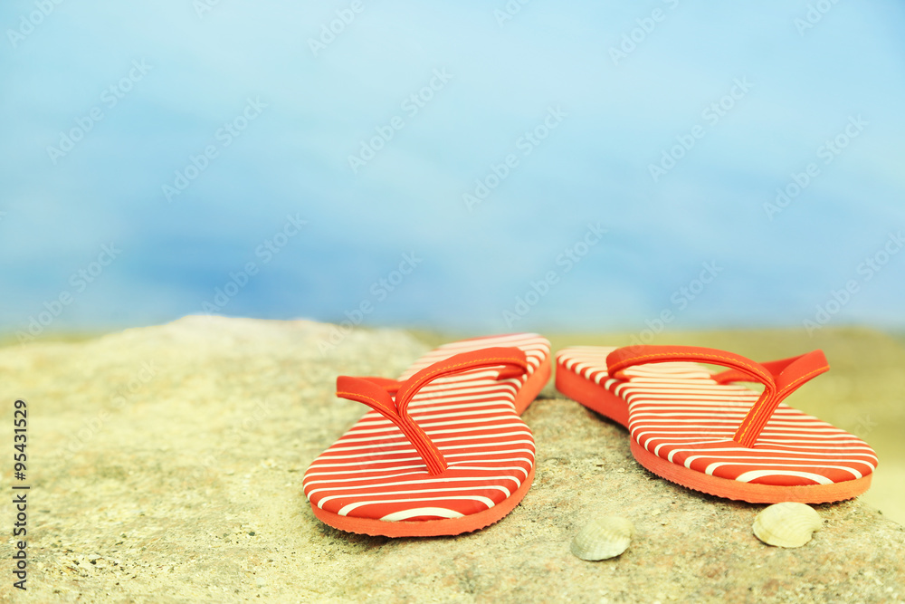 Naklejka premium Bright flip-flops on stone, nature background