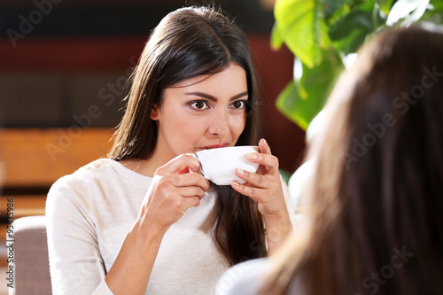 Tablou pe pânză Beautiful girls drink coffee and speaking in cafe