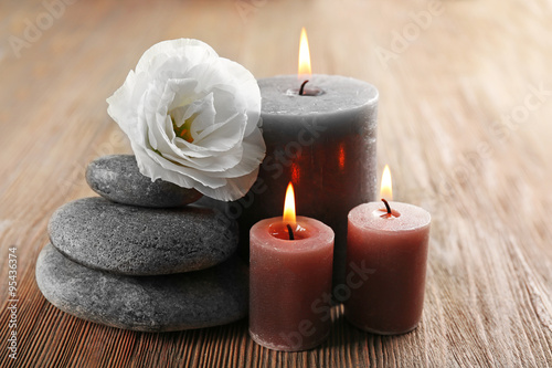 Aroma candle with pebbles and flower on wooden background
