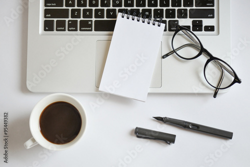 Coffee cup, spiral notebook, computer keyboard, and pen on white