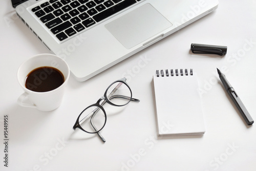 Coffee cup, spiral notebook, computer keyboard, glasses, and pen
