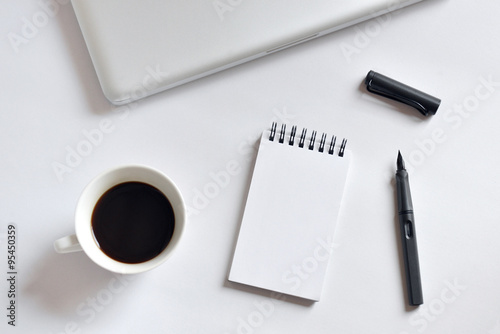 Coffee cup, spiral notebook, laptop, and pen on white background