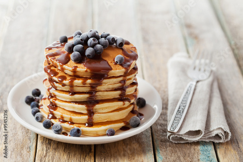 Stack of baked pancakes or fritters with chocolate sauce and frozen blueberries in a white plate on a wooden rustic table, delicious dessert for breakfast
