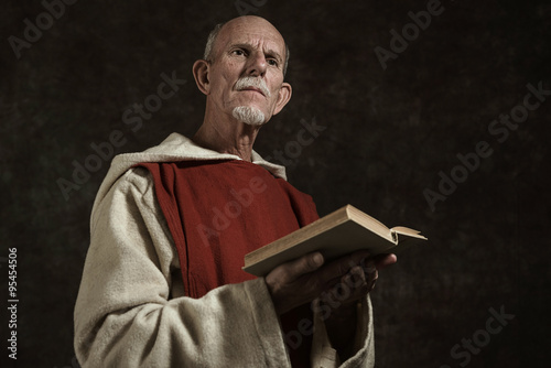 Foto Official portrait of monk holding book. Studio shot against dark