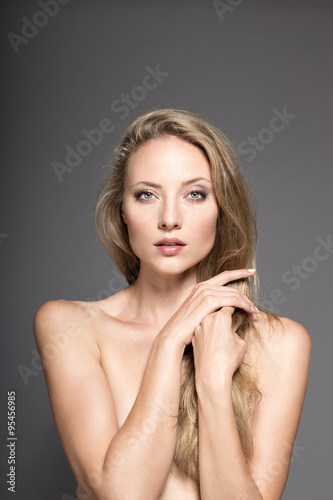 Awesome caucasian attractive sexy professional fashion model with blond hair posing in studio topless, perfect make up, tanned skin, isolated on gray background, retouched image