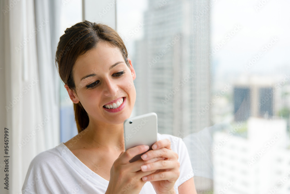 Woman texting on smartphone at home near the window.