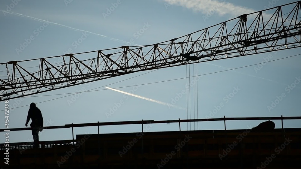 Construction workers silhouettes with construction cranes silhouetted against blue sky Construction workers silhouettes with construction cranes silhouetted against blue sky