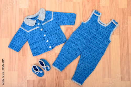 Baby boy winter clothes lying on the floor. Child knit wool jumpsuit set with sweater and shoes arranged, blue wardrobe for toddler. photo