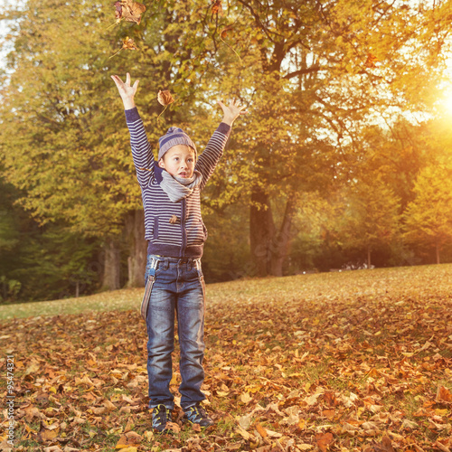 Young boy in autumn throwing some leaves in the air