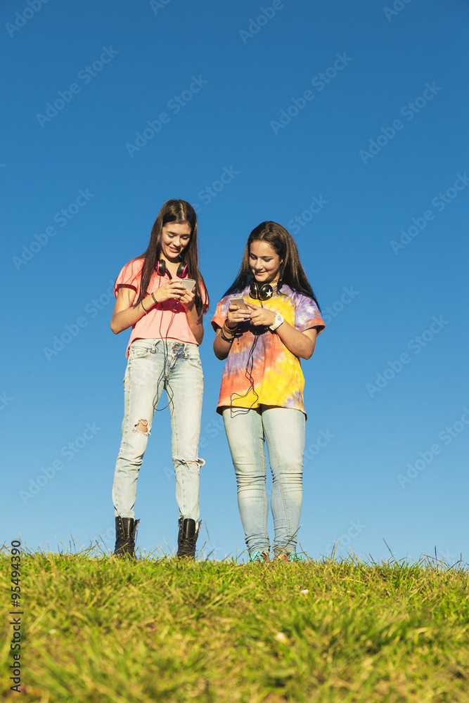 Two Teenage Girls Using Mobile In Park Two Teenage Girls Using Mobile In Park