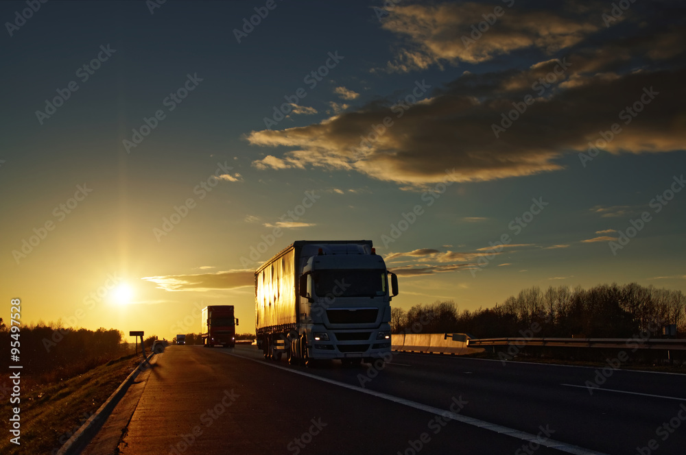 Trucks on asphalt highway in a rural landscape at sunset. Trucks on asphalt highway in a rural landscape at sunset.