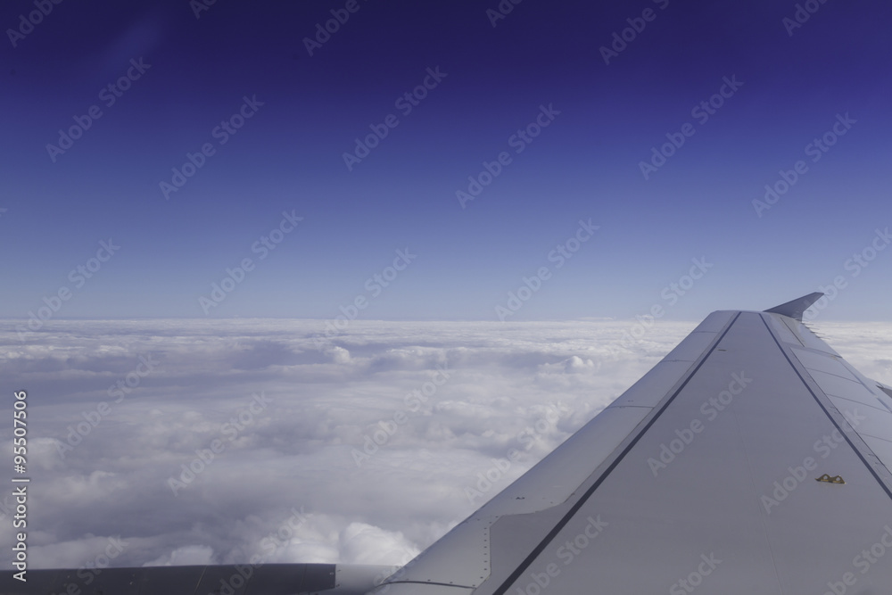 Fototapeta premium Wing of airplane above the clouds in the sky, view from window.